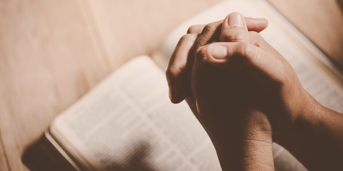 Clasped hands resting in prayer over an open Bible, illustrating the call to pastoral confession and honest dependence on God.