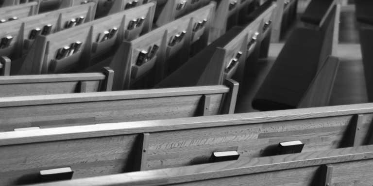Rows of empty wooden church pews, evoking the ancient baptismal setting where the Apostles' Creed was first confessed.