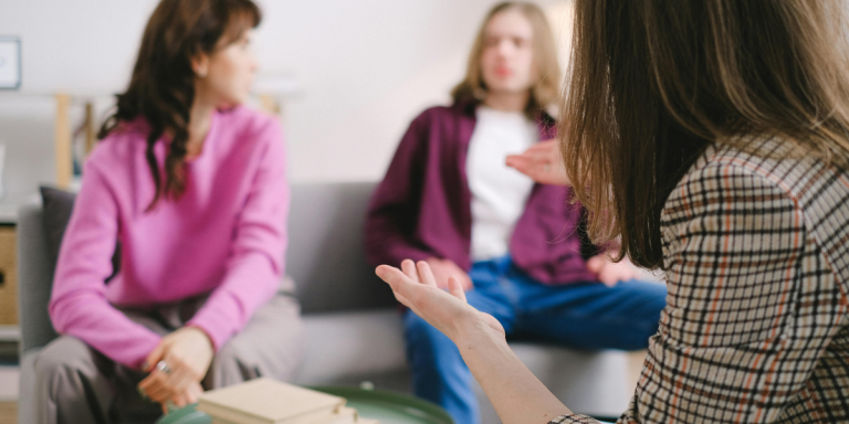 Three women seated together in unhurried conversation, one gesturing thoughtfully as the others engage — an image of the slow, intentional work of staying present with those we disagree with rather than walking away.
