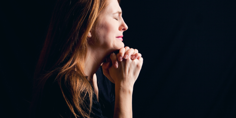 Woman praying with hands clasped and eyes closed, reflecting the practice of praying the imprecatory psalms to release bitterness and love enemies.