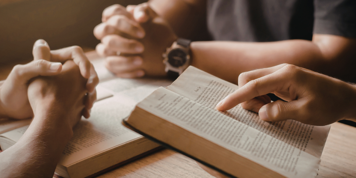 Two people studying an open Bible together, one pointing to the text, illustrating the authority and trustworthiness of Scripture.
