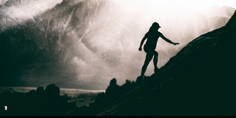 Silhouette of a person climbing a rocky ridge toward misty mountain peaks, evoking the persevering pursuit of character and spiritual formation explored in Matthew Arbo's The Pursuit of Character.
