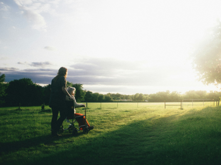 Michael and Tracy Balboni explore how Christians should care for the sick and dying in Walking Lois Home, A young caregiver gently holds the hands of an elderly woman in a wheelchair